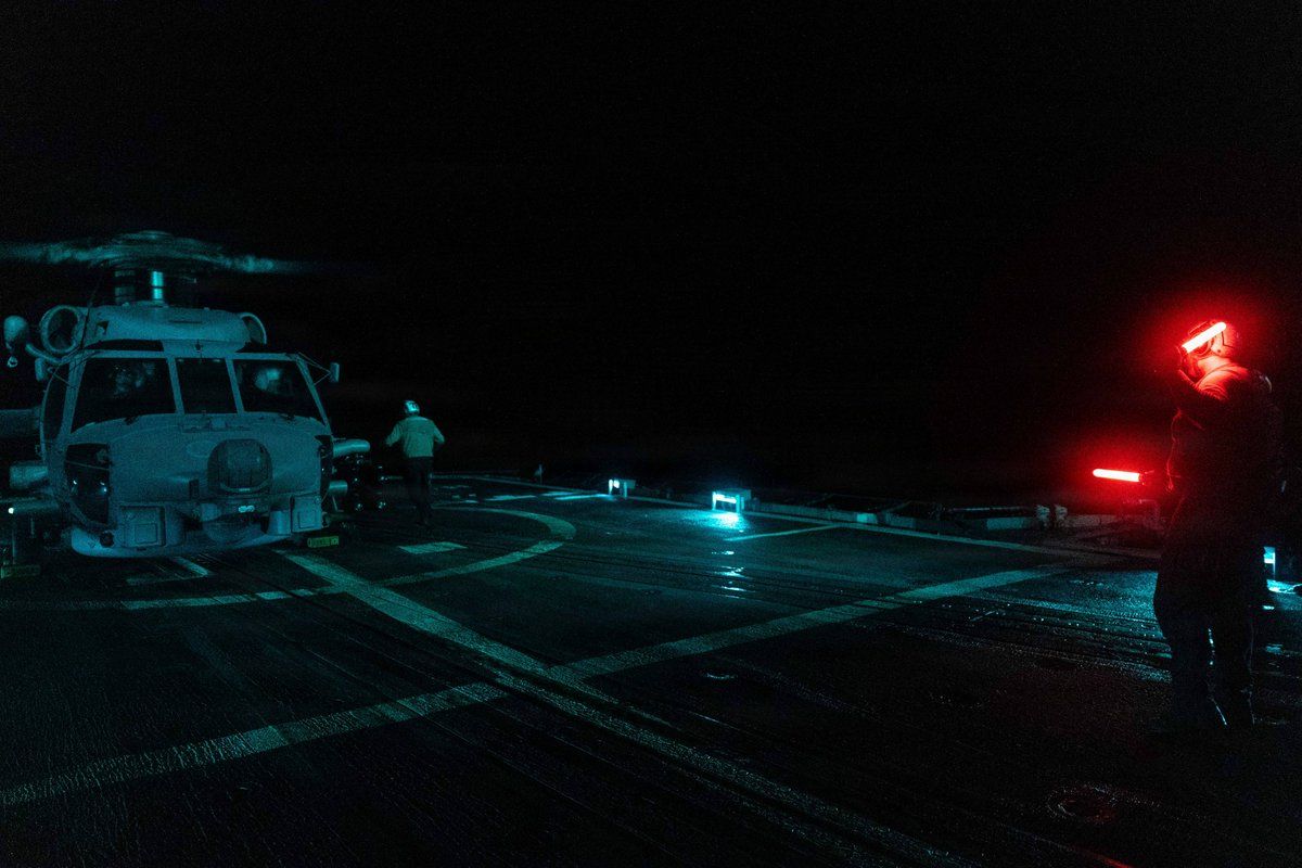 @U.S. Central Command: A U.S. Sailor directs an MH-60R Sea Hawk helicopter during nighttime flight operations aboard guided-missile cruiser USS Princeton (CG 59) as the ship sails in the Arabian Sea and enforces the U.S. bl